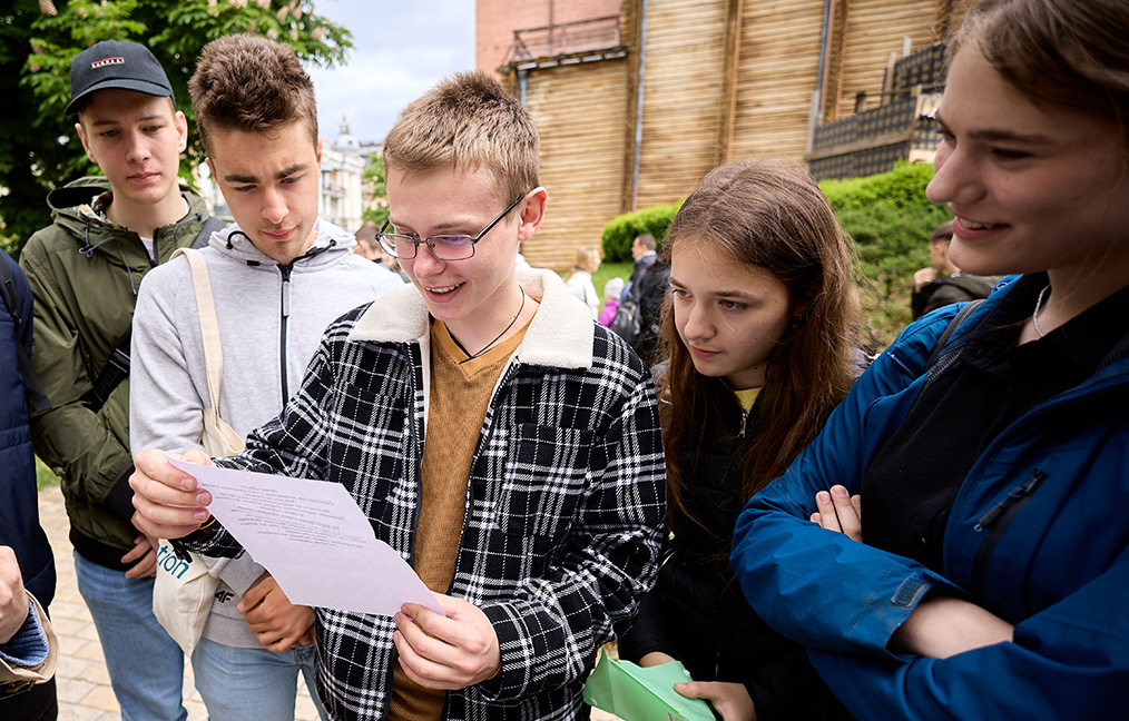 Young people watching their friend read a document, and he is smiling