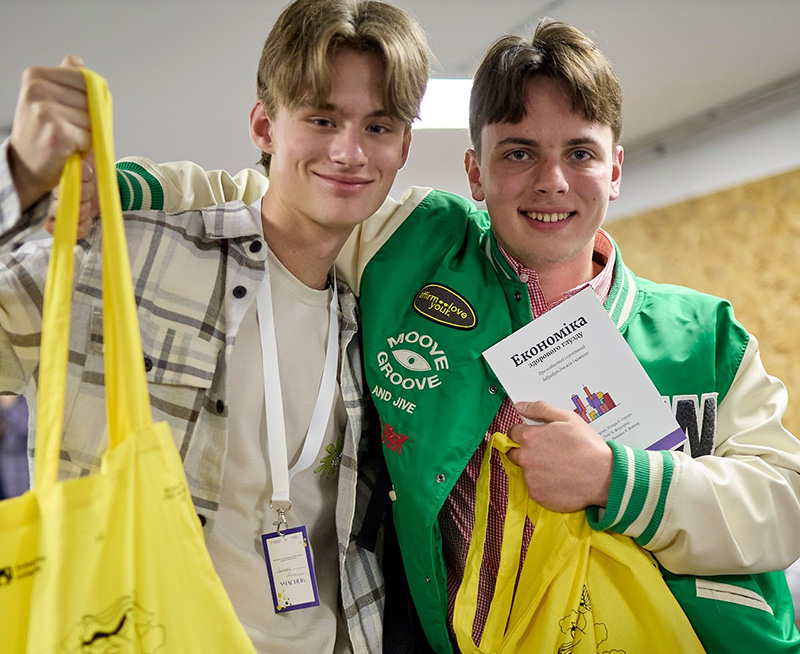 students holding up Common Sense Economics book and smiling at camera