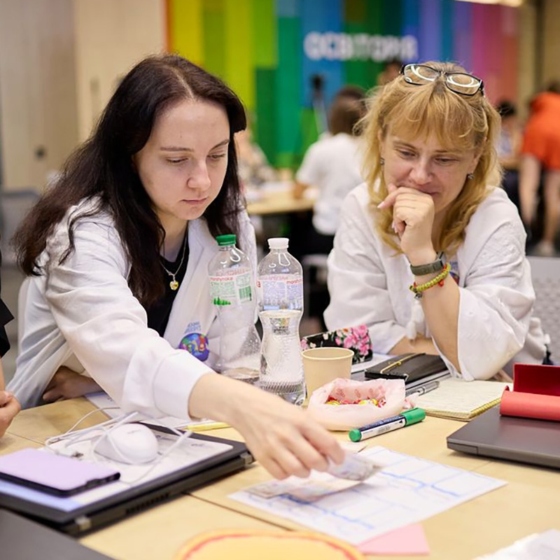 Two teachers collaborating together at a desk in a workshop, looking at reading materials